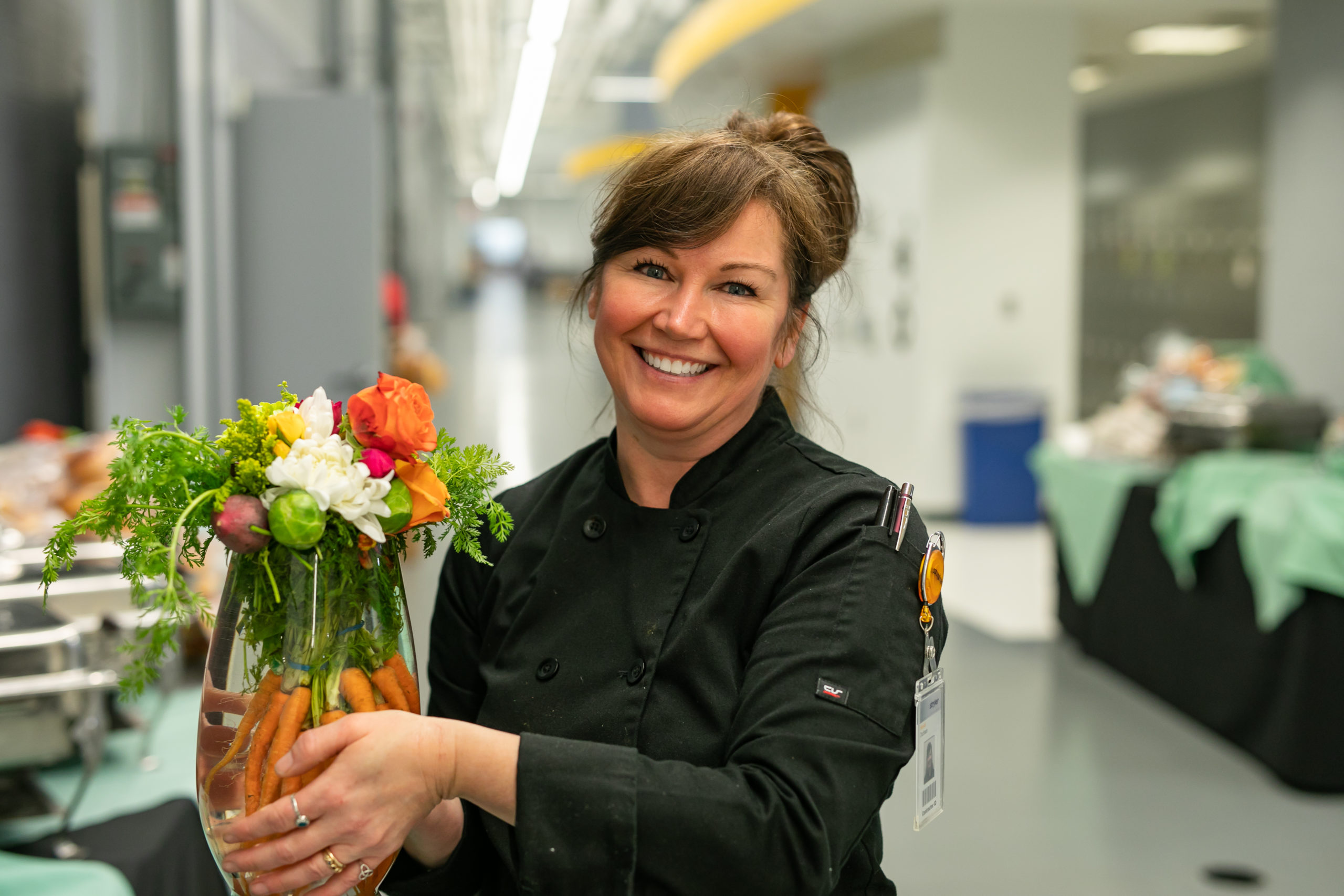 Creative Dining Employee Smiling Holding Vase With Flowers and Vegetables